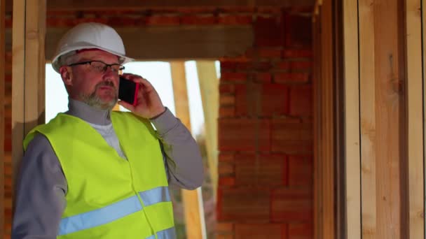土木技術者建築家の専門家は、建設現場での作業を制御するために携帯電話について話す — ストック動画