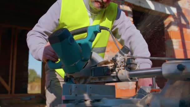 Тесляр використовує круглу електричну пилку для різання дерев'яних дощок, деревообробник на будівельному майданчику — стокове відео