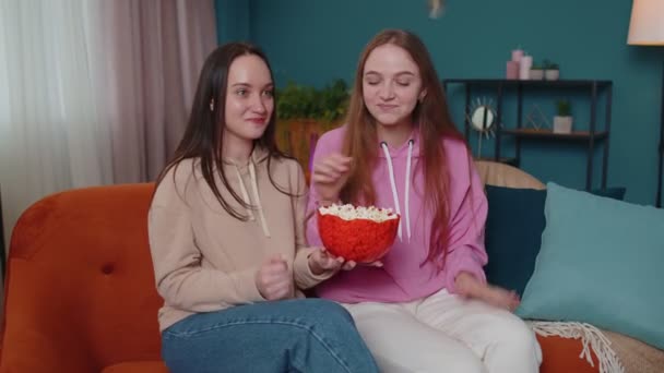Lányok barátok testvérek néz kedvenc TV show film és eszik popcorn, ül a kanapén otthon — Stock videók