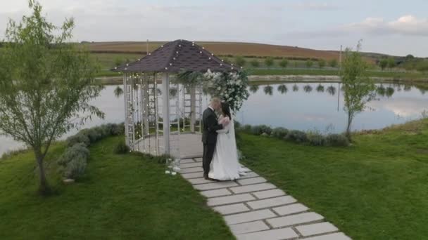 신혼 부부, 신랑, 신부 포옹, 포옹, 키스, 결혼 예식, 꽃으로 장식된 아치 — 비디오