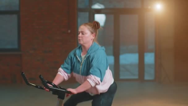 Gezonde blanke vrouw die traint op een stationaire fiets in de sportschool, slow motion — Stockvideo