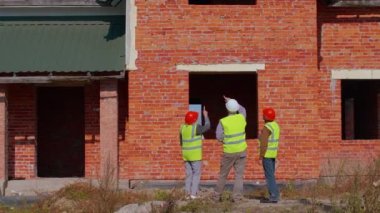 İnşaat binasının planlarıyla proje çalışmalarını tartışan kıdemli inşaat mühendisleriyle mimar.