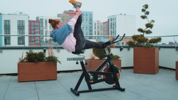 家の屋根の上で自転車固定自転車で有酸素トレーニングツイン演習を実行するアスレティックガール — ストック動画