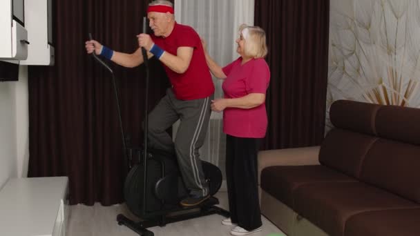 Hombre mayor en ropa deportiva usando orbitrek en la sala de estar haciendo ejercicios de entrenamiento deportivo de cardio en casa — Vídeo de stock