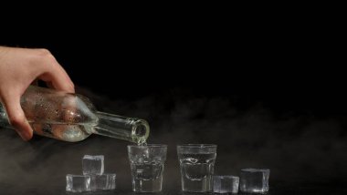 Barmen siyah arka planda bardaklara buz küpleriyle iki shot votka dolduruyor.