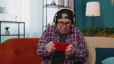 Evde cep telefonuyla online video oyunu oynayan yaşlı ve komik büyükbaba endişeli.