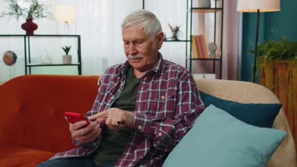Με χαρά ανώτερος παππούς άνθρωπος κατέχουν smartphone, ενθουσιασμένος για το κινητό app αθλητισμού στοίχημα νίκη προσφορά στο σπίτι — Αρχείο Βίντεο