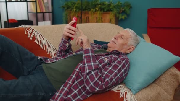 Büyükbaba cep telefonunu online alışveriş için kullanıyor, büyük bir zafer kazandı, evde kutluyor. — Stok video