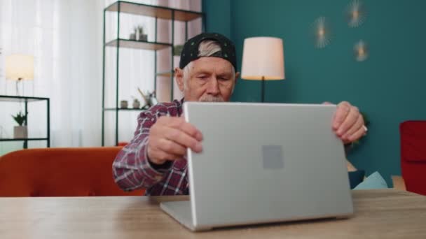 Abuelo de edad avanzada comienza a trabajar en el ordenador portátil, envía mensajes, hace compras en línea en casa — Vídeos de Stock
