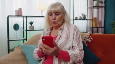 Şaşırmış büyük anne cep telefonu kullanıyor, iyi haber mesajı alıyor ani zaferle şok oluyor.