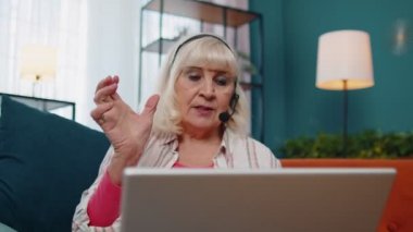 Kıdemli yaşlı kadın, kulaklık takıyor, video görüşmesi yapıyor, ev bilgisayarında ders veriyor.