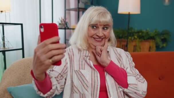 Feliz abuela mayor sosteniendo teléfono inteligente viendo videollamadas móviles en línea haciendo selfie casa — Vídeos de Stock