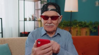 Büyükbaba cep telefonunu online alışveriş için kullanıyor, büyük bir zafer kazandı, evde kutluyor.