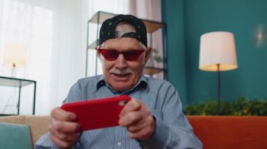 Evde cep telefonuyla online video oyunu oynayan yaşlı ve komik büyükbaba endişeli.
