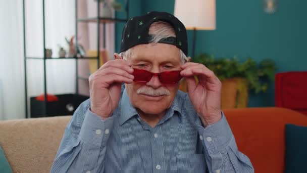 Elegante abuelo con gorra de marihuana, con gafas de sol rojas, mirando a la cámara con una sonrisa encantadora — Vídeos de Stock