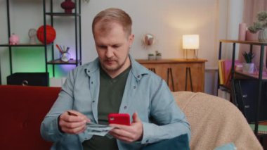 Adam evde oturup kredi kartı ve akıllı telefon kullanarak online alışveriş yapıyor.