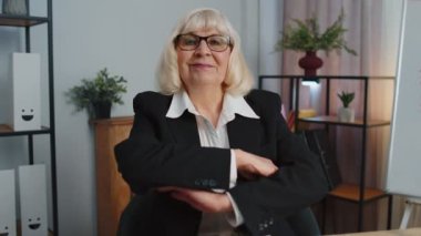 Neşeli yetişkin ofis kadını gözlük takıyor, resmi takım elbise giyiyor, gülümsüyor, kameraya bakıyor.