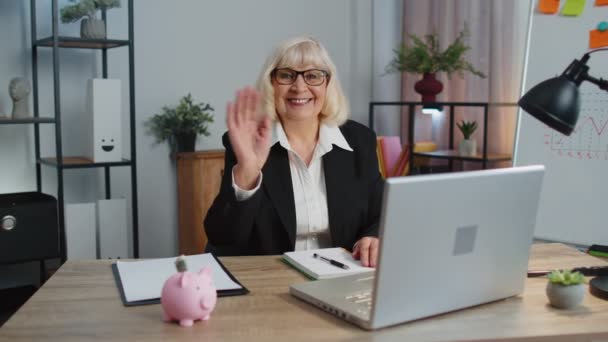 Старша бізнес-леді хвилі руку долоні в привіт жест вітає когось вебінар в домашньому офісі — стокове відео