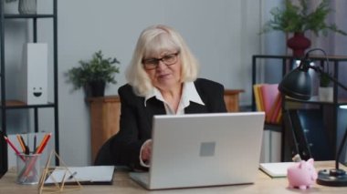 Sinirli yaşlı iş kadını masaya yumruğuyla vuruyor, arızalı laptoplu bilgisayarı kapatıyor.