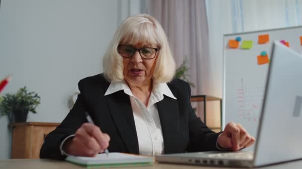 Senior elderly business office woman elearning online writing notes from laptop, live webinar online — Vídeos de Stock