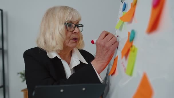Anciana anciana mujer de negocios entrenador conferencia altavoz analizando infografías dibujar en pizarra de oficina — Vídeos de Stock