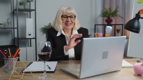 나이든 여성 프리랜서 가 사무실 책상에 앉아 노트북 PC pc 를 만들다가 와인을 마시고 있습니다. — 비디오