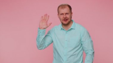 Sakallı adam kameraya dostça gülümsüyor ve el sallıyor.