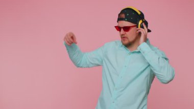 Neşeli çekici adam kulaklıkla müzik dinliyor ve dans edip eğleniyor.