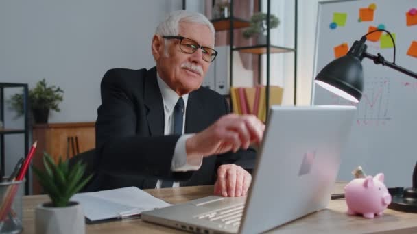 Senior zakenman viert eenzame verjaardag op kantoor, blaast kaarsen op kleine taart doet een wens — Stockvideo