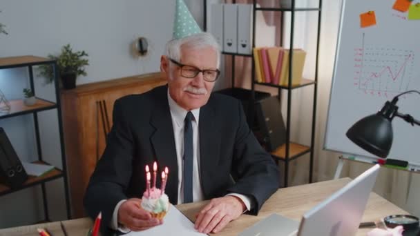 Senior oude zakenman viert verjaardag in kantoor met kleine taart met kaarsen die een wens doen — Stockvideo