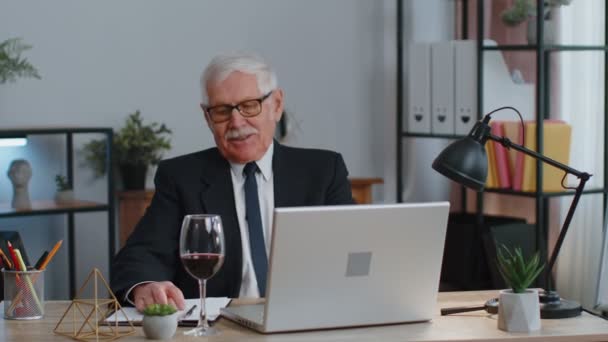 Idős férfi szabadúszó bort iszik, miután dolgozott laptop számítógép PC ül íróasztal az irodában — Stock videók