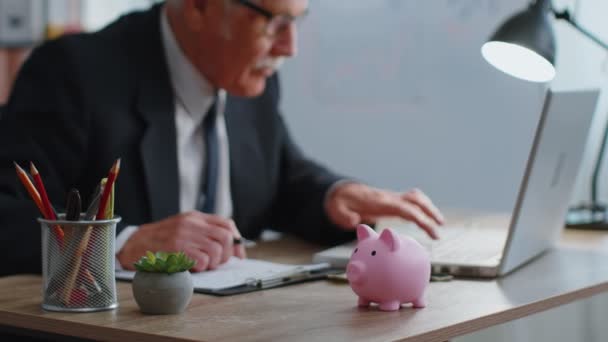 Piggy bank, senior business man účetní psaní na notebooku výpočtu příjmu z peněz — Stock video