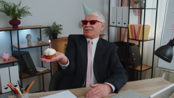 Senior businessman celebrating lonely birthday in office, blowing candle on small cake making a wish — ストック動画