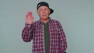 Kıdemli adam kameraya dostça gülümseyip el sallayarak merhaba ya da hoşça kal diyor.