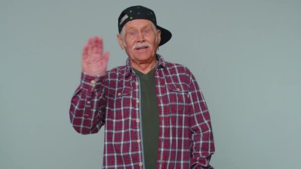 Senior man smiling friendly at camera and waving hands gesturing hello or goodbye, welcoming — Stockvideo