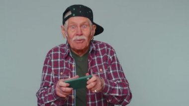 Endişeli, komik, bağımlı, yaşlı bir adam cep telefonuyla yarış oyunları oynuyor.