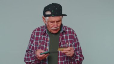 Para transferi sırasında kredi kartı ve akıllı telefon kullanan kıdemli bir adam internetten alışveriş yapıyor.