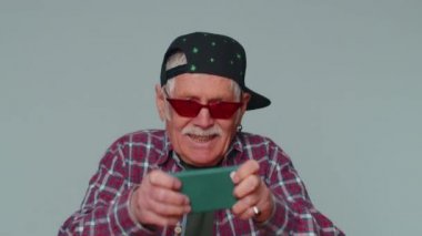 Endişeli, komik, bağımlı, olgun bir adam cep telefonuyla yarış oyunları oynuyor.