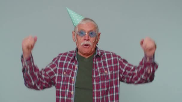 Wesoły pozytywny senior w stożkowym kapeluszu świątecznym, taniec, zabawa, świętowanie urodzin — Wideo stockowe