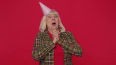 Cheerful positive senior woman in cone festive hat, dancing, having fun, celebrating birthday party