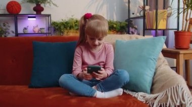 Happy little school kid girl use mobile cell phone play online game, celebrate big win, good news