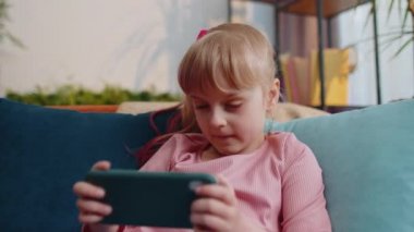 Worried teen child girl kid enthusiastically playing racing video online games on smartphone at home