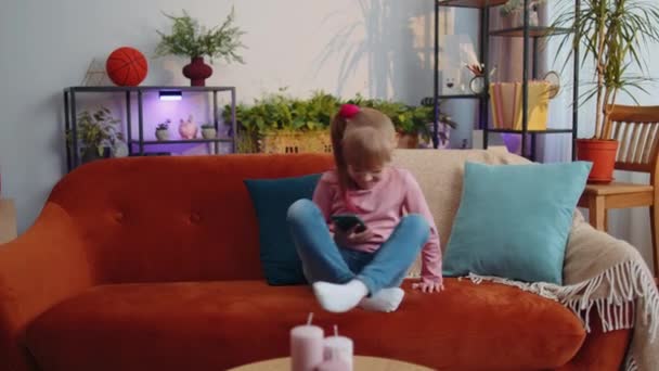 Bambino bambino tenere smartphone guardando cartoni animati divertenti, chiacchierando con gli amici sul divano da solo a casa — Video Stock