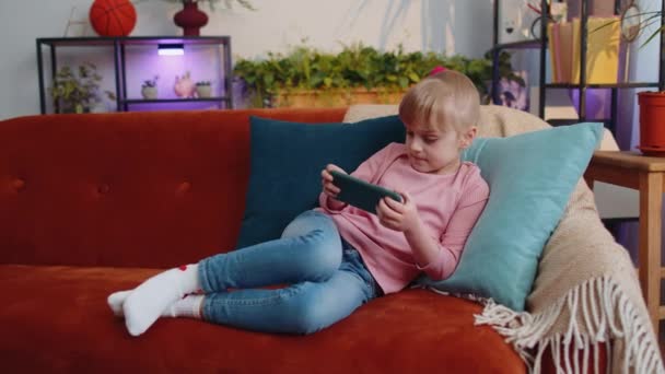 Ανησυχία έφηβος παιδί κορίτσι ενθουσιωδώς παίζει αγωνιστικά βίντεο online παιχνίδια στο smartphone στο σπίτι — Αρχείο Βίντεο