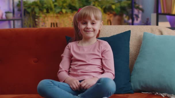 Alegre linda caucasiana menina criança criança sorrindo, olhando para a câmera sentada no sofá em casa — Vídeo de Stock