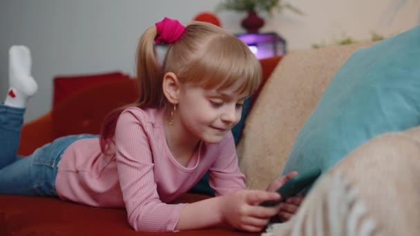 Bambino bambino tenere smartphone guardando cartoni animati divertenti, chiacchierando con gli amici sul divano da solo a casa — Video Stock