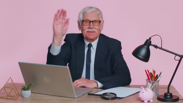 Senior business man waves hand palm in hi gesture greeting welcomes someone webinar at pink office — Stockvideo