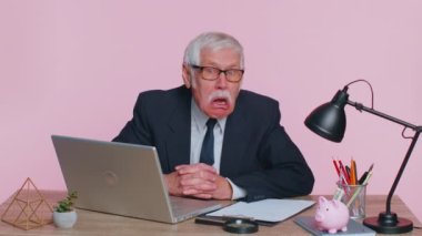 Senior mature older office businessman working on laptop computer, making funny face, fooling around