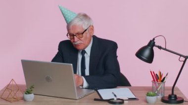 Sad upset lonely senior businessman celebrating birthday party alone, holds cake at pink office