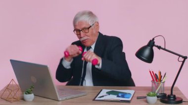 Kıdemli iş adamı egzersiz yapıyor, kol kaslarını şişiriyor pembe dambılları kaldırıyor, işten sonra dinleniyor.